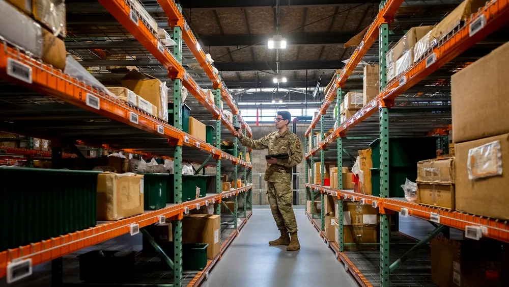 Air Force supply technician scanning inventory on shelves in a warehouse aisle